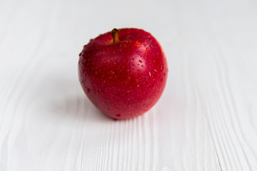 Single red apple on white wooden surface close