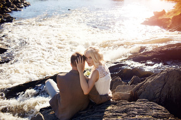 Couple in love close-up sitting on a stone on a beautiful Sunny day at sunset. Love emotions and hugs in the sun. Blonde woman and man with beard look at each other