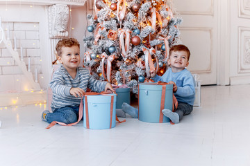 Little and cute twins brothers in front of the christmas tree  unwrapping gifts and having fun. New year's eve. Cozy holiday at the fir-tree. love, happiness and big family concept