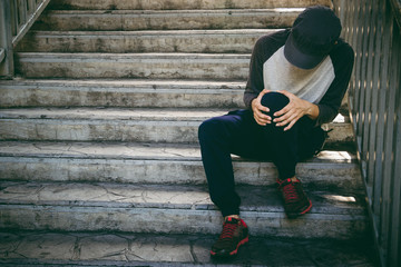 Fototapeta premium Runner man a knee pain. Young man holding knee with his hands in pain after free free running.