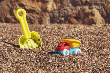 Children's toy truck with gravel or sand. Yellow scoop on the background. Concept of transportation of goods and building materials. Industrail symbols. Summer holiday by the sea.