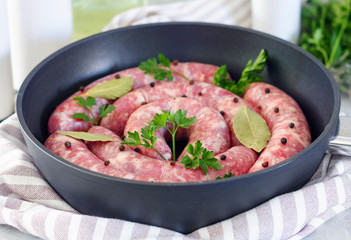 Meat sausages in frying pan, with bay leaves and fresh herbs in the kitchen