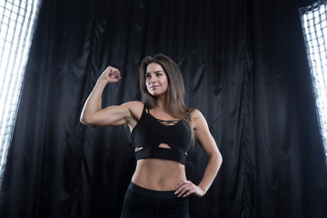 Fitness model in black sports uniform posing on a dark background