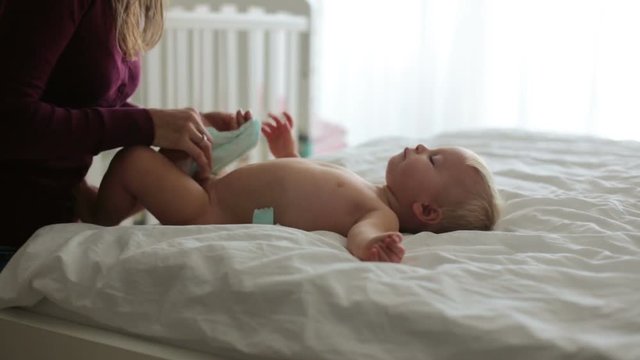Young mom, changing baby diaper after bath in sunny bedroom
