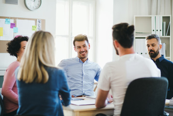 Group of young businesspeople sitting around table in a modern office, having meeting.
