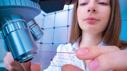 Young woman technician is examining a histological sample, a biopsy in the laboratory of cancer research