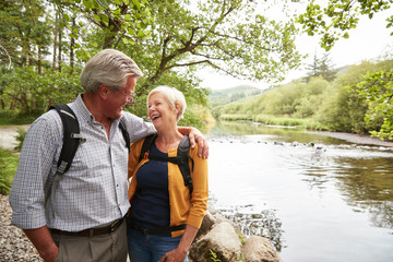 Senior Couple Hiking Along Path By River In UK Lake District