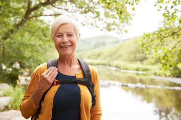 Portrait Of Senior Woman Hiking Along Path By River In UK Lake District