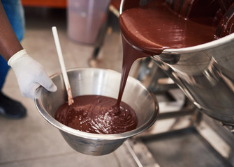 Melted chocolate pouring into a bowl in confectionary factory