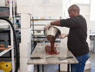 Worker pouring melted artisanal chocolate out on a factory table