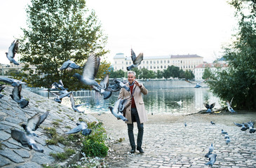 Mature businessman walking by river Vltava in Prague city, dispersing pigeons.