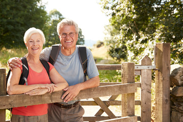 Portrait Of Senior Couple Hiking In Lake District UK Looking Over Wooden Gate