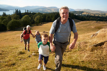 Grandparents With Grandchildren Climbing Hill On Hike Through Countryside In Lake District UK...