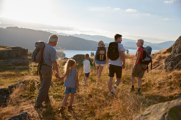 Rear View Of Multi Generation Family Walking On Top Of Hill On Hike Through Countryside In Lake...