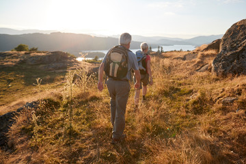 Rear View Of Senior Couple Walking On Top Of Hill On Hike Through Countryside In Lake District UK