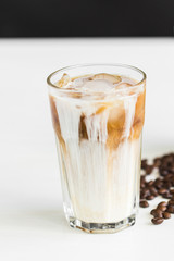 Ice coffee in a glass with cream over and coffee beans on the table