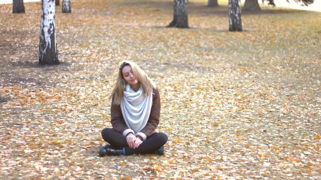 Girl on the street.
Girl sits on the ground and meditates alone with her eyes closing. She enjoys being surrounded by trees.
