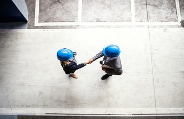 A top view of an industrial man and woman engineer in a factory, shaking hands.
