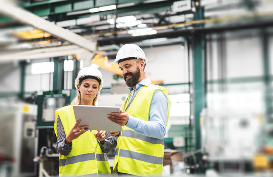 A portrait of an industrial man and woman engineer with tablet in a factory, talking.