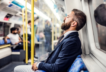 Sleeping hipster businessman inside the subway in the city, travelling to work.