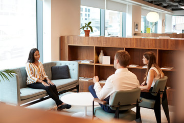 Businessman And Businesswoman Interviewing Female Candidate In Office At Graduate Recruitment Assessment Day