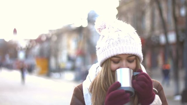 Girl on the street.
Girl drinks hot drink. She looks great with her fabulous smile. Eyes looks down, wind blows in the face. Winter.