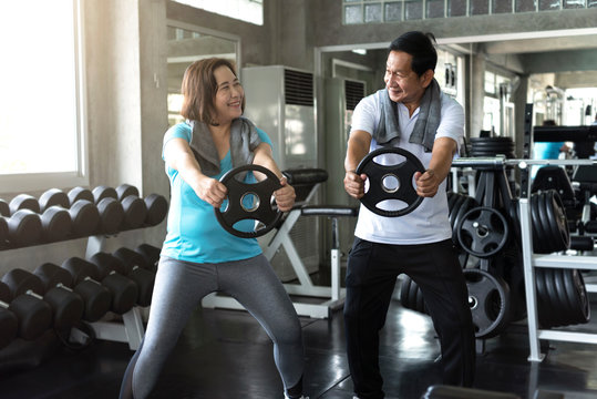 Asian Senior Man And Woman Exercise Lifting Dumbbell In Fitness Gym. Elderly Healthy Lifestyle.