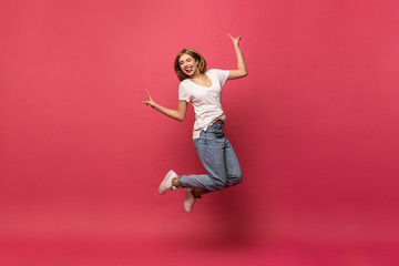 happiness, freedom, motion and people concept - smiling young woman jumping in air over pink...