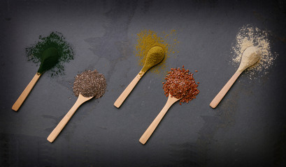Wooden spoons on a slate backdrop, with piles of seeds and supplemnets.
