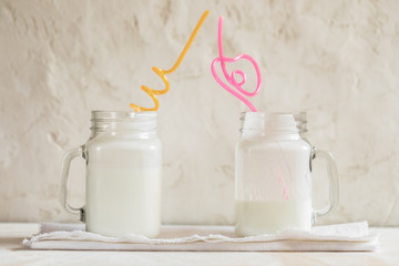 Two glass jars with kefir and colored drinking tubes on white background.