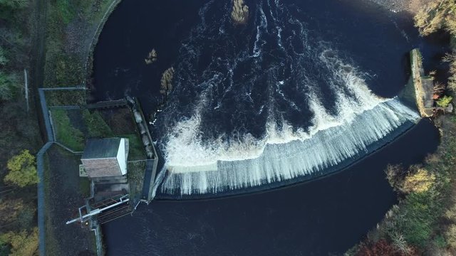 Aerial footage looking directly down on Blantyre Weir and fish ladder on the dark waters of the River Clyde.