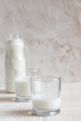 Two glasses and bottle with kefir are standing on white table on white background.