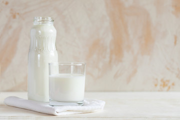 Glass bottle and glass with kefir are standing on napkin on white table on white background.