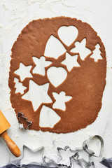 Gingerbread dough with various shape cookie cutout. Baking background for baking Christmas gingerbread cookies. Top view of cookie dough with cutters and rolling pin on white marble table.