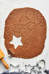 Gingerbread dough with various shape cookie cutout. Baking background for baking Christmas gingerbread cookies. Top view of cookie dough with cutters and rolling pin on white marble table.