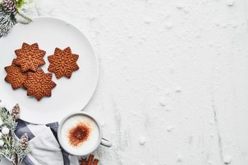Gingerbread cookies with hot cocoa drink or eggnog on white marble table covered with snow. Top...