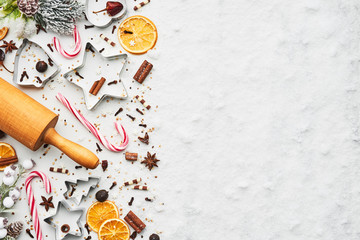 Obraz na płótnie Canvas Holiday baking background for baking Christmas cookies with cutters, rolling pin, candy cane and spices on white marble table covered with snow. Top view with copy space for text.