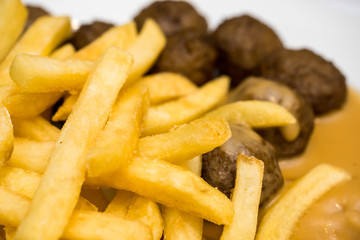 Delicious meatballs with peas, sauce and french fries in a white dish. Close-up. Shallow depth of field.