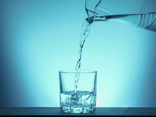 Pour water from a pitcher into a glass. Drinking water is poured from a jug into a glass on a blue background.