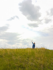 a young woman with red hair and a blue denim dress is in the mountains outside the city and is trying to catch a cellular connection.