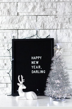 Happy new year darling words made with white letters on a black board with Christmas tree on  white brick wall background