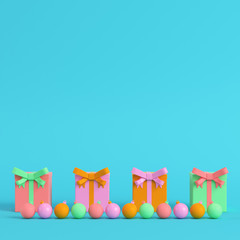 Naklejka premium Four colorful gift boxes with ribbon bow and christmas ball on bright blue background in pastel colors on bright blue background in pastel colors