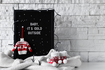 Baby it's cold outside phrase made with white letters on a black wooden board with knitted sweaters and cute decorations