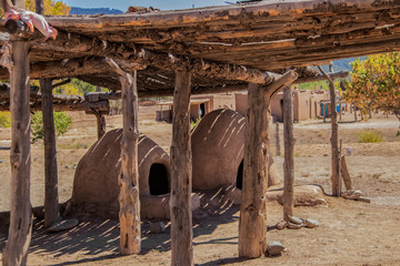 Two hornos-traditional earthen ovens- underneath a drying rack with a childs doll left on the corner - Homes of the Ute Pueblo in Taos New Mexico in the background - shallow focu