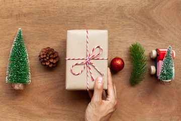 A man hands holding parcel post gift box with christmas decoration object on wooden table. Concept of christmas holiday celebration and new year. Top view