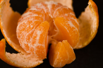 Juicy orange tangerine with peel and slices lies on a black background
