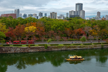 OSAKA PERFECTURE, JAPAN-NOVEMBER 9, 2018: Visitors  on a tram and cruise boat enjoying autumn season colours at Osaka Castle Park in Osaka, Japan.