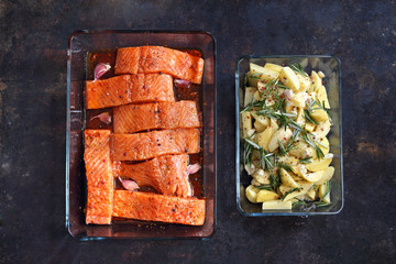 Ryba z frytkami. Składniki potrawy. Surowy filet z łososia i pokrojone ziemniaki z ziołami, ułożone w naczyniach do pieczenia.