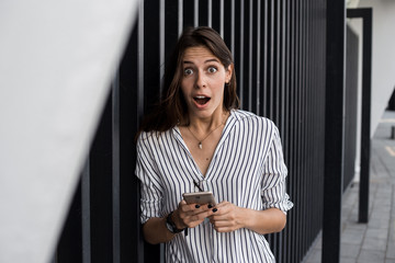 Fototapeta na wymiar Overjoyed young woman reading message from friend on mobile expressing happiness about great news,emotional female excited with winning discount for shopping while walking in downtown