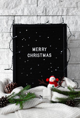 Merry Christmas phrase made with white letters on a black board with knitted sweaters and Christmas decorations on white background